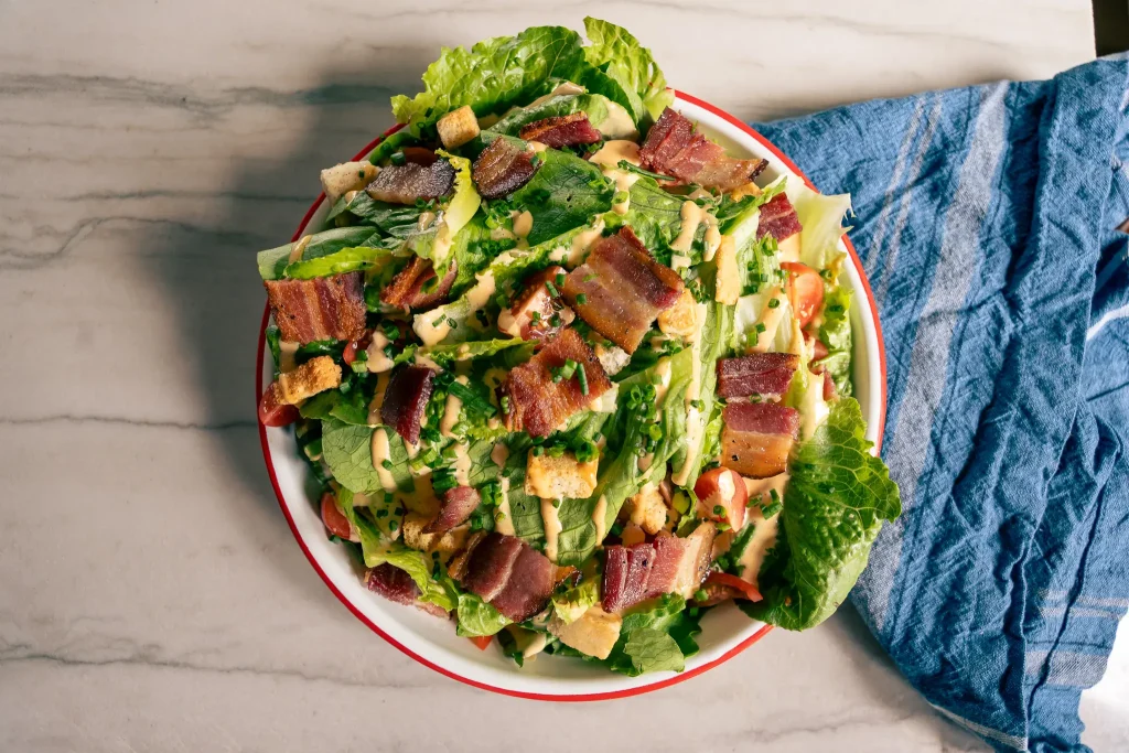 BLT Salad | Carnation Farms Romaine lettuce salad topped with crispy bacon, croutons, and creamy dressing on a white plate with a red rim