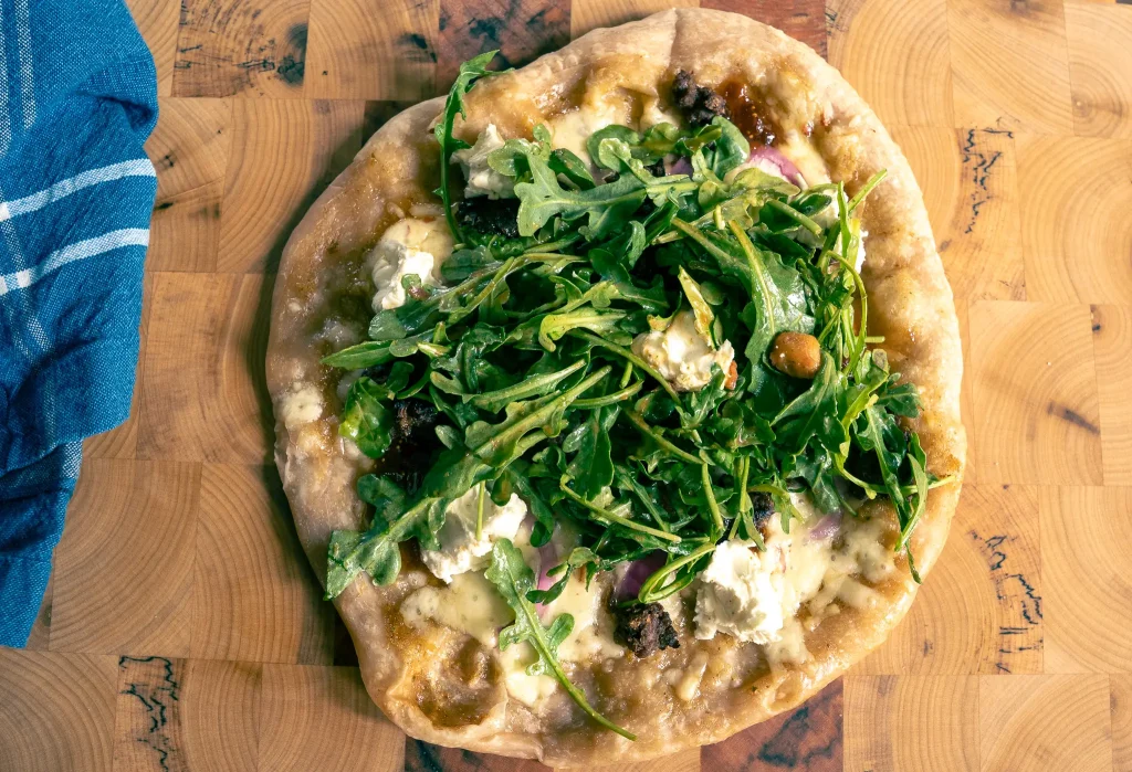 Pizza topped with fresh arugula, melted cheese, and onions on a rustic wooden board