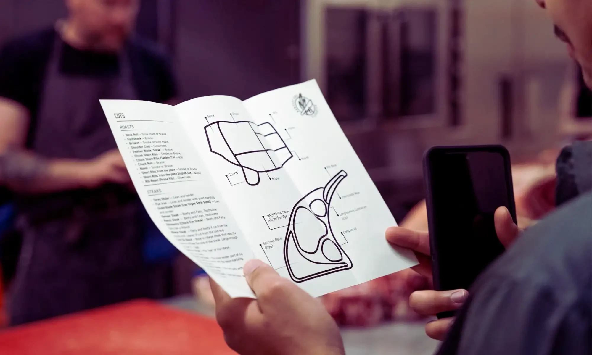 Close-up of a person holding a brochure with a large mechanical diagram; a smartphone is in the foreground.